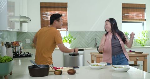 Couple dancing while cooking on sunlit kitchen island with fresh salad bowls for healthy moments