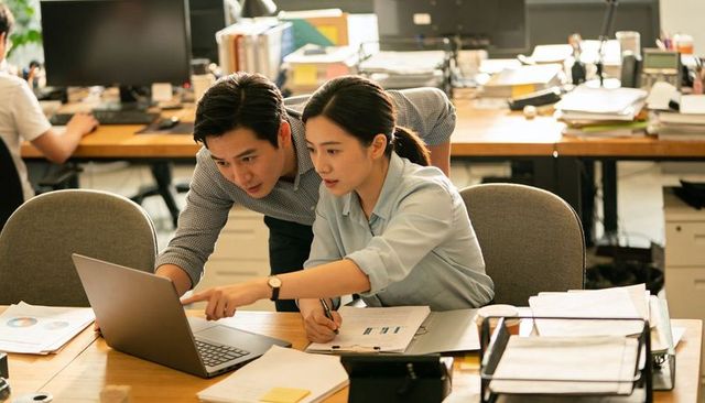 Coworkers collaborating and analyzing laptop charts in open-plan office workspace