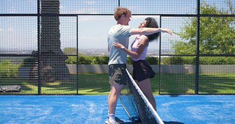 Young couple embracing over net on bright blue outdoor racket court during sunny day