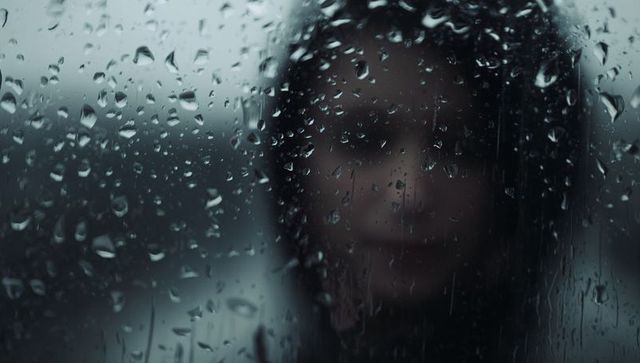 Moody Silhouette of Woman Behind Rain-Soaked Window