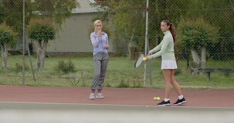 Tennis coach supervising young player practicing forehand on outdoor red court