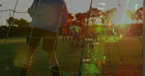 Goalkeeper bracing behind net at sunset with sports analytics data overlay