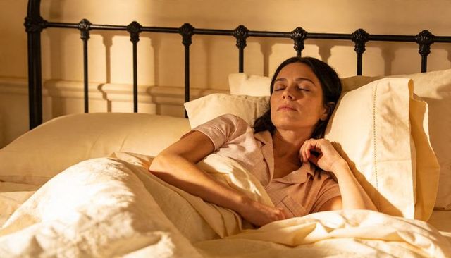 Tranquil woman resting in warm cozy bed with cream linens and vintage iron headboard
