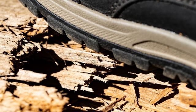 Close-up hiking shoe sole pressing into dry shredded bark on sunlit trail