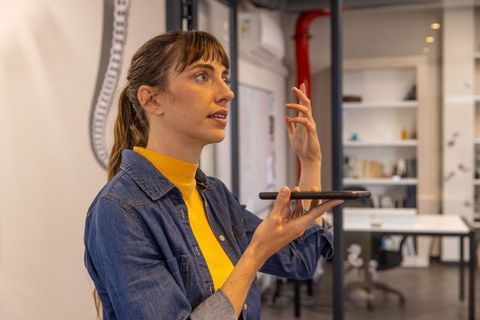 Mid adult woman using voice command on smartphone in modern office