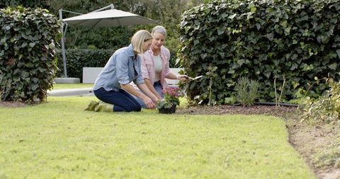 Mother and Daughter Planting Pink Flowers in Backyard Garden Kneeling Together