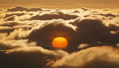 Golden sun rising through thick cloud layers over sea of clouds at dawn