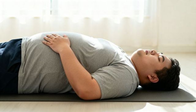 Overweight man practicing deep breathing on yoga mat at home in bright sunlit space