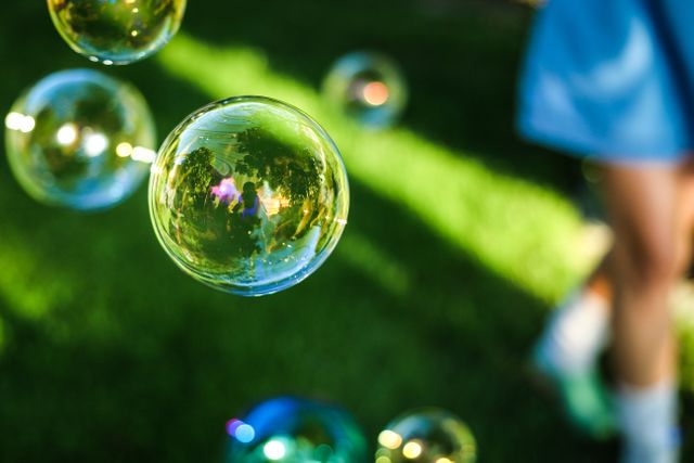 Soap bubbles floating through the air in a sunny park. Ideal for themes of childhood, playfulness, and outdoor summertime activities. Perfect for advertisements about outdoor toys, children's activities, family fun, and summer events.