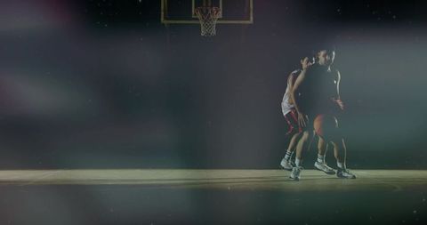 Moody cinematic basketball players dribbling and defending under spotlight on indoor court