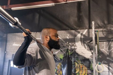 African man lifting loaded barbell in graffiti warehouse gym showing strength and focus