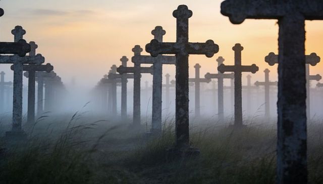 Misty cemetery at sunrise with weathered stone crosses standing in rows, moody memorial