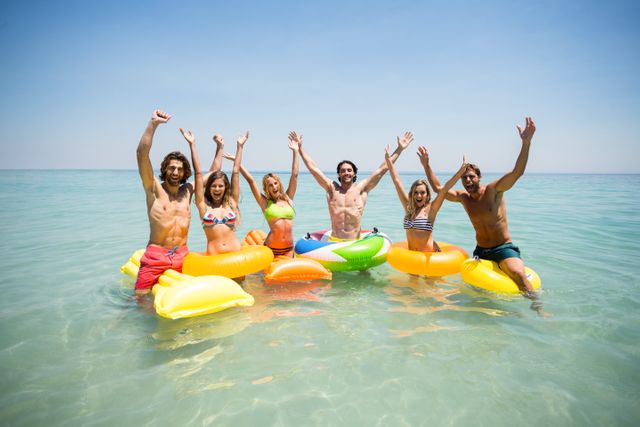 Portrait of cheerful friends enjoying on inflatable rings and pool rafts in sea against sky