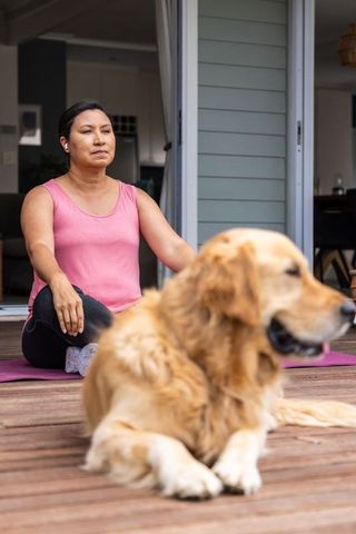 Mature woman meditating on home deck with earbuds and golden retriever companion