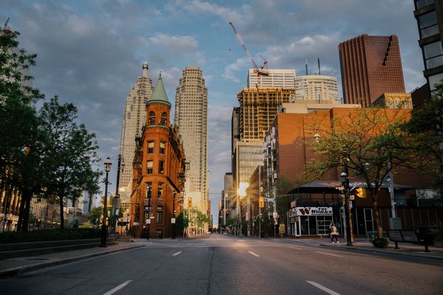 Street in downtown Toronto featuring a historic building with a pointed roof juxtaposed against modern glass skyscrapers. Suitable for visuals conveying city life, architecture contrasts, urban planning, or Toronto-related travel content.