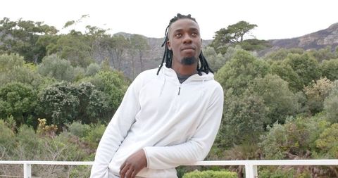 African-American man leaning on white railing overlooking rocky ridge and lush forest