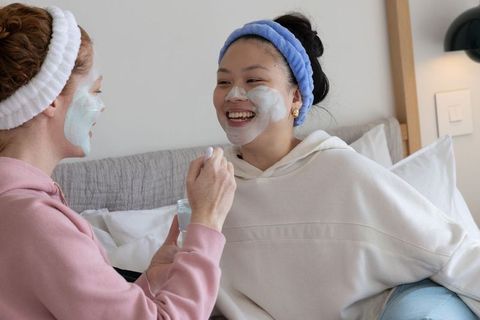 Multicultural friends sharing face mask and laughing during cozy at-home spa night