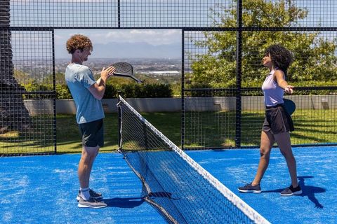 Diverse couple clapping and stretching on blue padel court, sunlit outdoor urban sport