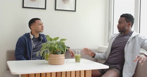 Diverse male friends talking over green juice in cozy dining nook, casual conversation