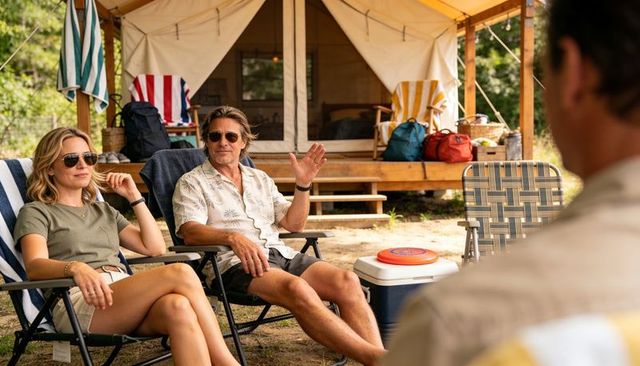 Couple relaxing in sunglasses by glamping tent with cooler, backpacks and towels