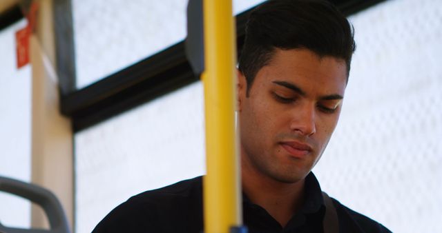 Young man traveling on a public bus, looking focused and contemplative. Ideal for use in articles and advertisements about urban transportation, commuting challenges, bus travel experiences, or solo journeys in a city.