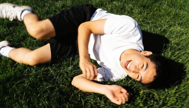 Smiling teen rolling on lush green lawn wearing white t-shirt and black athletic shorts