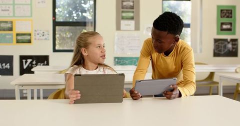 Diverse classmates collaborating with tablets in modern classroom learning environment