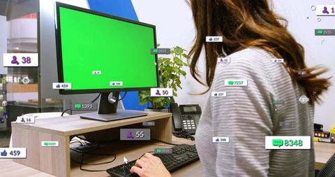 Woman turning toward green-screen monitor showing social analytics overlays on office workstation
