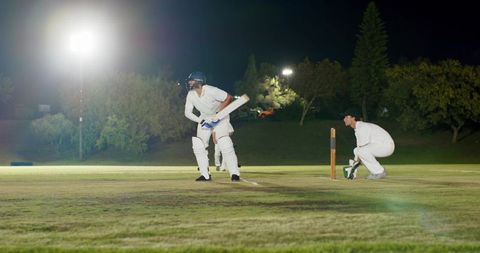 Night cricket under floodlights batsman batting crease with wicketkeeper crouching
