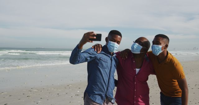 Three family members wearing masks taking a selfie at the beach. Ideal for themes on pandemic lifestyle, family bonding, safe social activities, and outdoor fun.