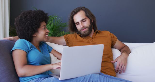 Biracial couple sitting on sofa using laptop in living room. staying at home in self isolation during quarantine lockdown.