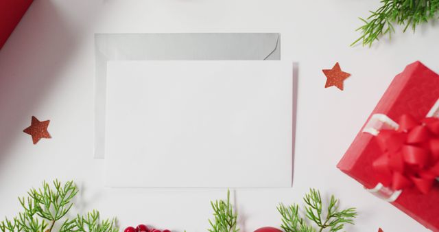 Top view of white holiday greeting card and envelope surrounded by festive Christmas decorations. This image can be used for holiday invitation designs, seasonal marketing promotions, or DIY craft project inspirations.