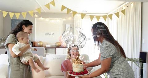 Family celebrating birthday with cake and balloons in bright daylit living room