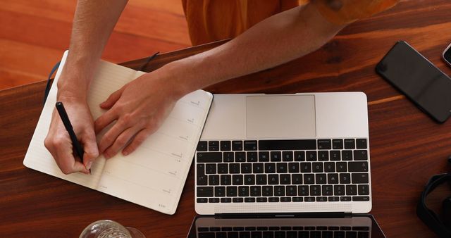 Hands Writing in Notebook on Wooden Desk with Laptop and Smartphone - Download Free Stock Images Pikwizard.com