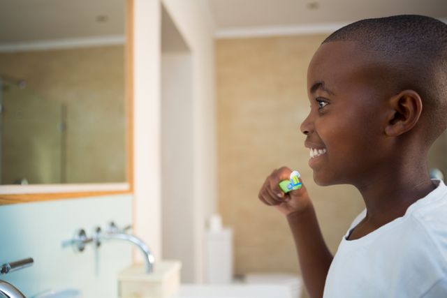 Young boy smiling while brushing teeth in bathroom. Ideal for promoting dental hygiene, children's health, morning routines, and personal care products. Suitable for educational materials, healthcare advertisements, and family lifestyle content.