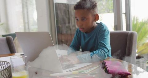 Young schoolboy concentrating on laptop, studying remotely at sunlit dining table