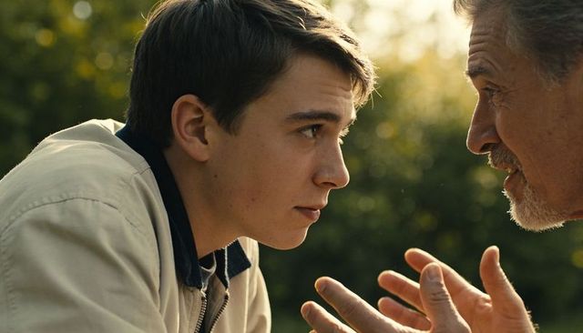 Teen listening intently to older man while leaning forward in sunlit park conversation
