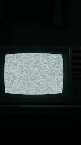 Vertical video of vintage CRT television displaying static noise in dark room evoking nostalgia