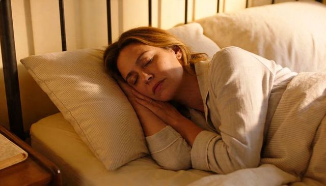 Sleeping peacefully woman in cozy bedroom with striped pillow, bedside book, soft warm light