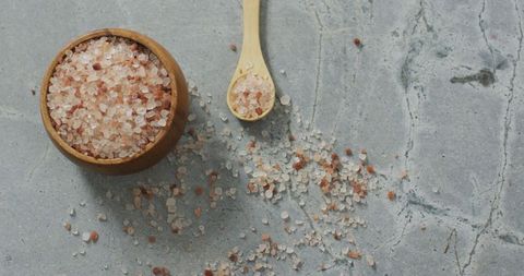 Himalayan pink salt in bowl with spoon on stone worktop