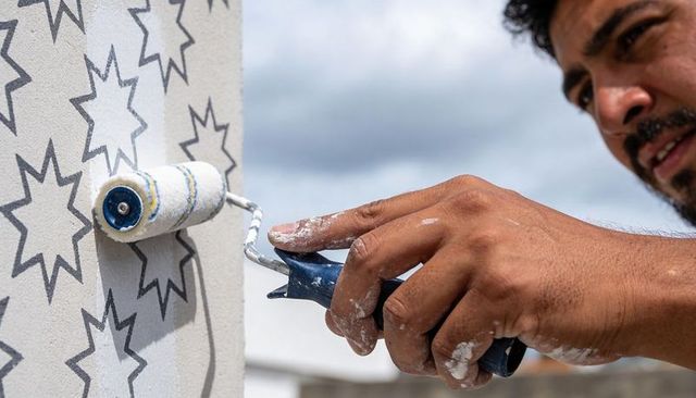 Rooftop painter rolling paint over star stencil on exterior wall, close-up hands