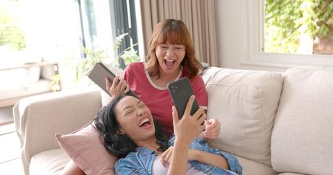 Joyful Young Women Relaxing with Smartphones at Home