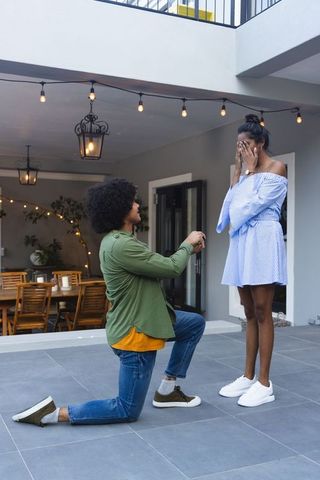 African american man proposing on tiled patio under string lights romantic engagement