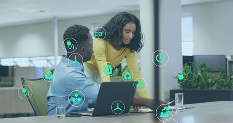 Business professionals collaborating on laptop with green energy icons for sustainability