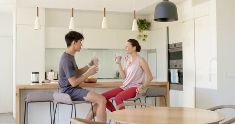 Multiracial couple sharing healthy smoothies at modern kitchen island and breakfast bar