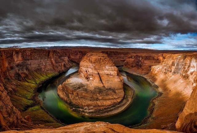 Dramatic cloudy sky looming over the iconic Horseshoe Bend in Arizona. Vivid landscape captures the unique horseshoe-shaped meander of the Colorado River amidst rugged cliffs and desert scenery. Ideal for use in travel blogs, adventure promotions, nature photography exhibitions, and geography educational materials.