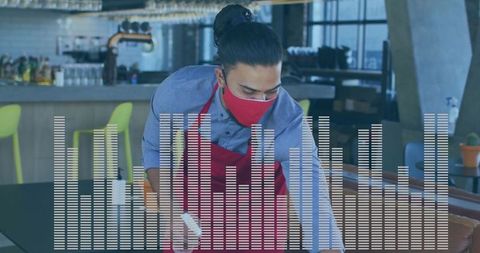 Masked staff cleaning dining table in bar with sanitizing spray