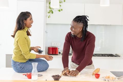 South asian and african american couple baking and laughing in bright modern kitchen