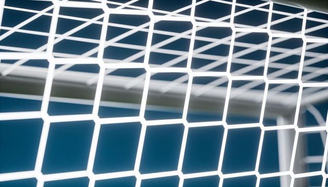 Closeup white hexagonal soccer net stretching across goal crossbar with blue background