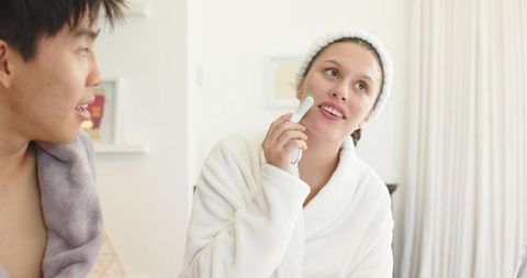 Diverse couple sharing morning skincare routine with facial device in modern bathroom